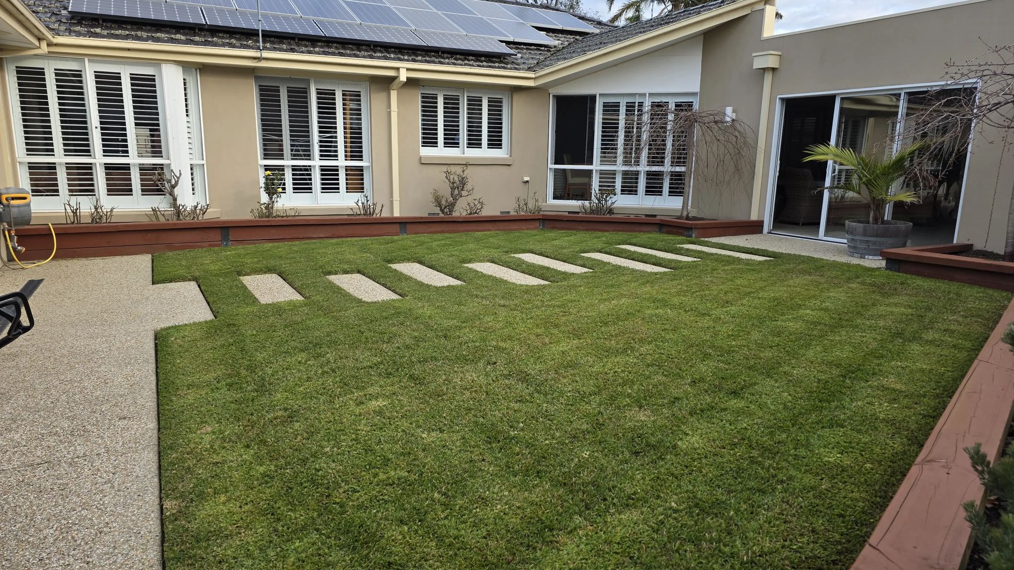 Freshly mown back lawn with stepping stones and clipped garden beds at a Frankston home maintained by Prestige Property Care